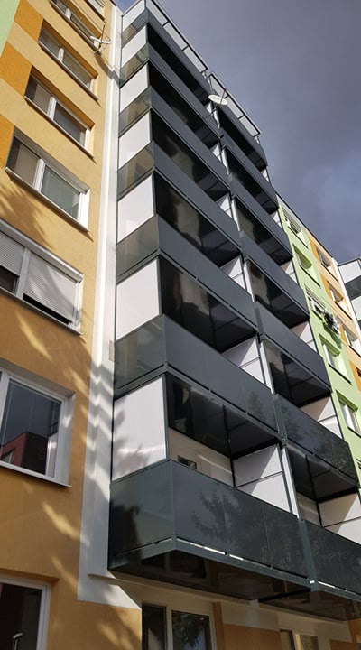 Antracitové zasklené balkóny na rohu bytového domu