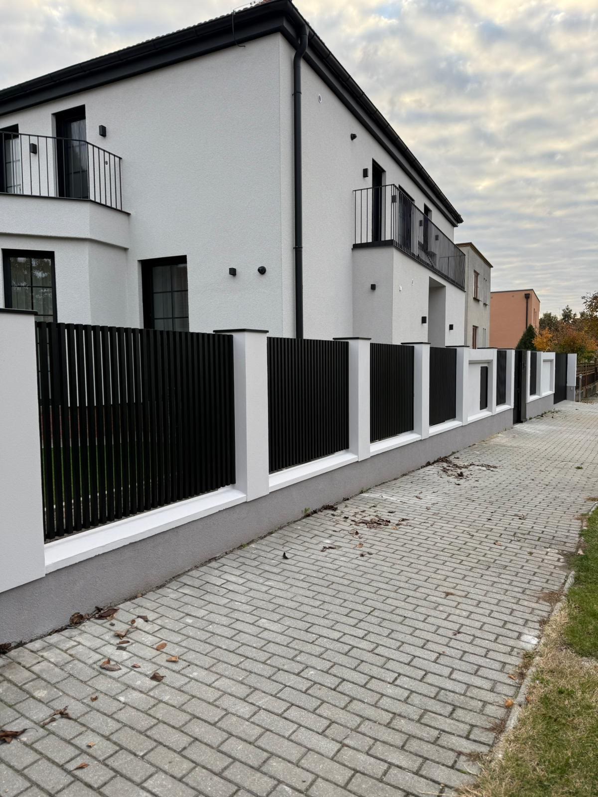 Rad čiernych lamelových výplní osadených medzi bielymi murovanými stĺpikmi