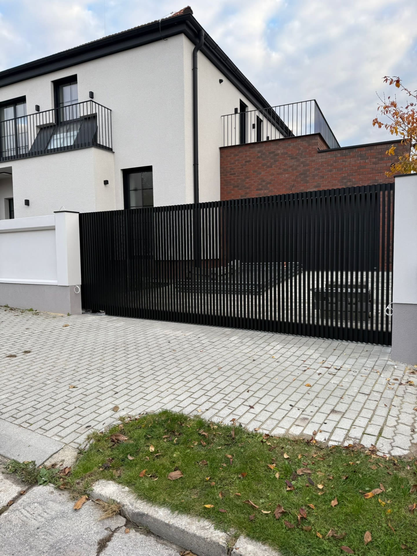 Čierne lamelové oplotenie s posuvnou bránou pri dlažbovom vjazde