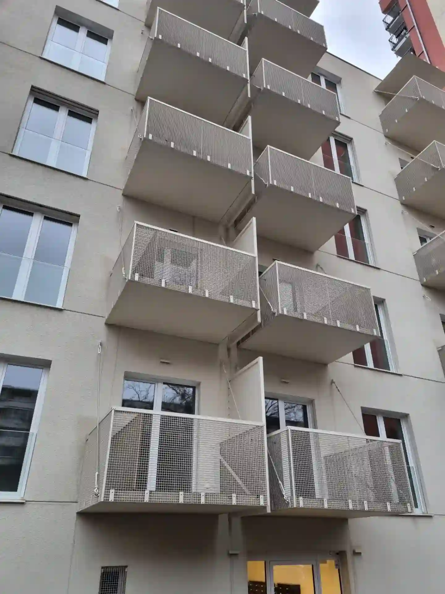 Predná fasáda bytového domu so závesnými balkónmi a lanovými závesmi