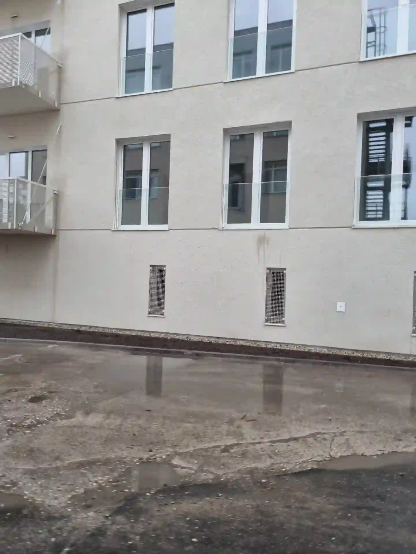 Dokončená fasáda bytového domu s balkónmi a vetracími mriežkami